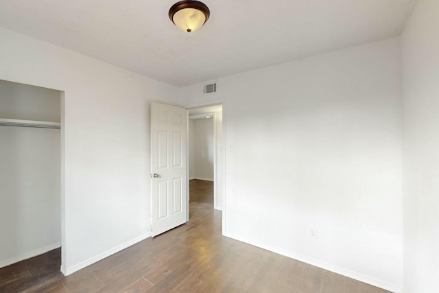 unfurnished bedroom with wood finished floors, visible vents, a closet, and baseboards