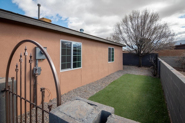 view of side of property featuring a lawn, a fenced backyard, and stucco siding