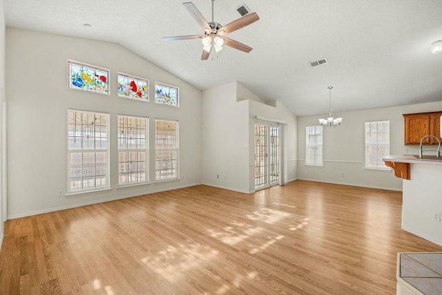 unfurnished living room with ceiling fan with notable chandelier, light wood-type flooring, and a healthy amount of sunlight