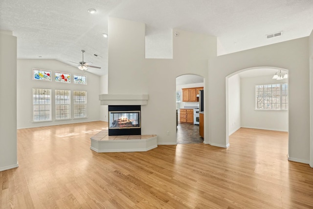 unfurnished living room with visible vents, a textured ceiling, light wood-style floors, a multi sided fireplace, and ceiling fan with notable chandelier