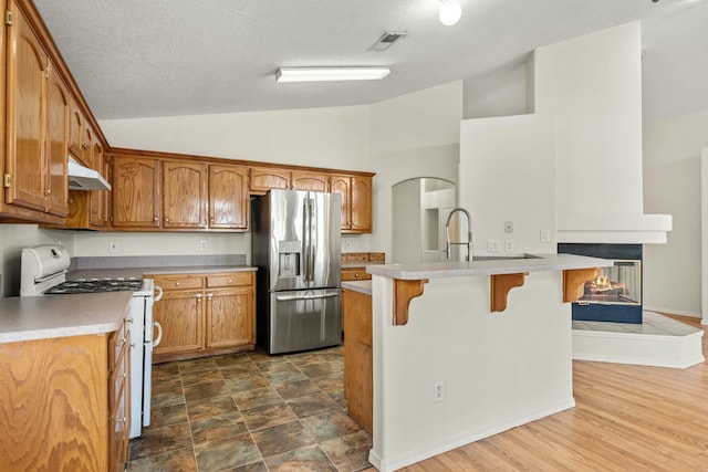 kitchen featuring gas range gas stove, visible vents, stainless steel fridge, under cabinet range hood, and a kitchen bar