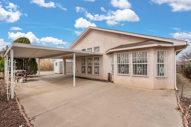 back of property featuring a storage shed, an attached carport, an outdoor structure, and stucco siding