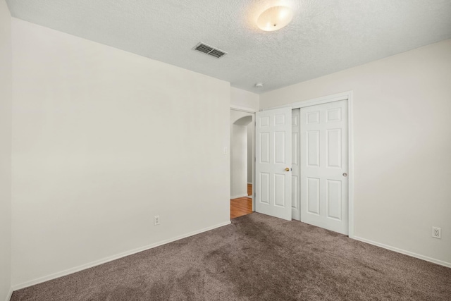 unfurnished bedroom with carpet floors, arched walkways, a closet, visible vents, and a textured ceiling