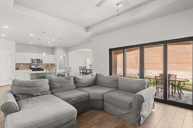 living room featuring visible vents, arched walkways, ceiling fan, light wood-style flooring, and a textured ceiling