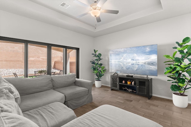 living room with ceiling fan, wood finished floors, visible vents, baseboards, and a tray ceiling