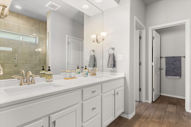 full bathroom with double vanity, a stall shower, visible vents, wood finished floors, and a sink