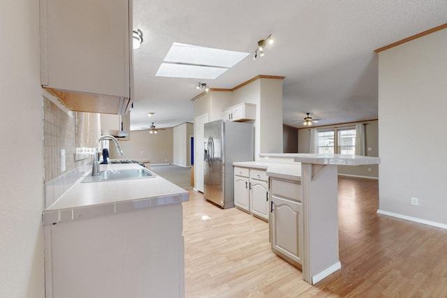 kitchen featuring a skylight, a sink, light wood-type flooring, stainless steel fridge, and a peninsula