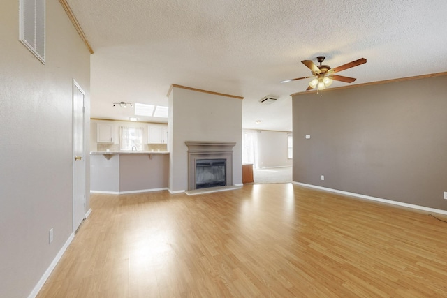 unfurnished living room with visible vents, a glass covered fireplace, ceiling fan, a textured ceiling, and light wood-style floors