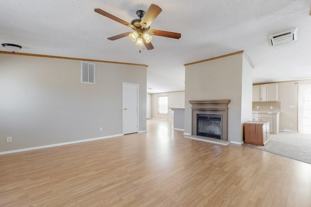 unfurnished living room featuring light wood-style flooring, visible vents, ceiling fan, and a glass covered fireplace