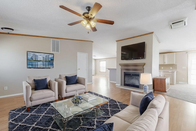 living area with light wood finished floors, visible vents, and a glass covered fireplace