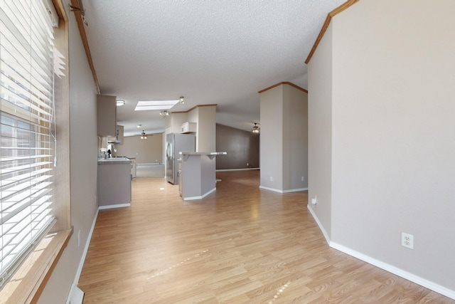 unfurnished living room with a textured ceiling, lofted ceiling, baseboards, light wood finished floors, and crown molding