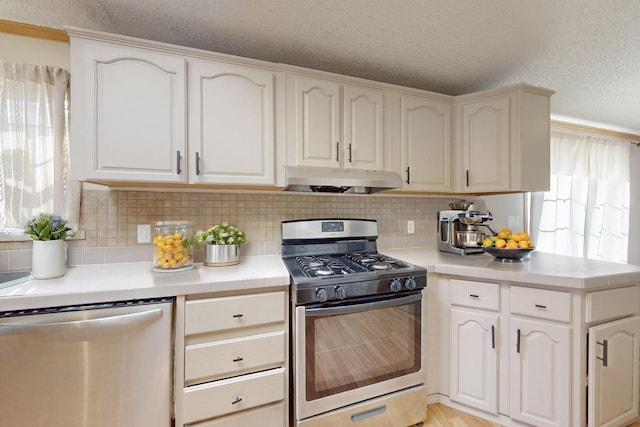 kitchen featuring appliances with stainless steel finishes, tasteful backsplash, a textured ceiling, and exhaust hood