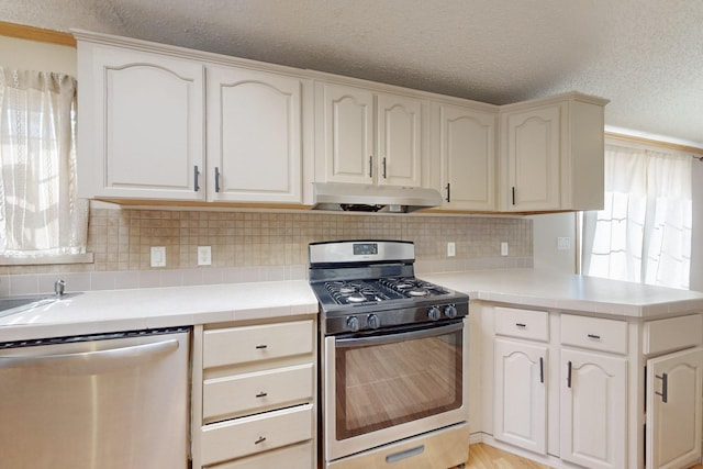 kitchen featuring a textured ceiling, stainless steel appliances, exhaust hood, tile counters, and tasteful backsplash