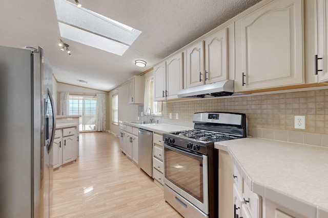 kitchen featuring lofted ceiling with skylight, appliances with stainless steel finishes, light countertops, under cabinet range hood, and a sink