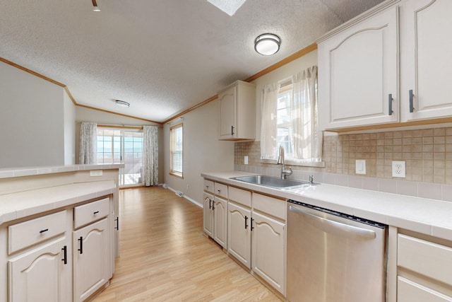 kitchen with light wood finished floors, lofted ceiling, crown molding, stainless steel dishwasher, and a sink