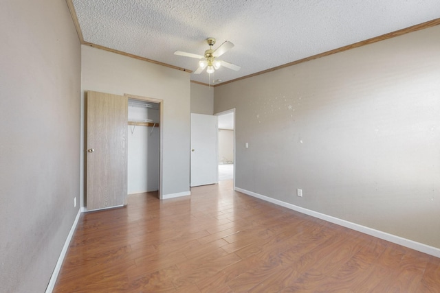 unfurnished bedroom featuring a textured ceiling, wood finished floors, baseboards, ornamental molding, and a closet