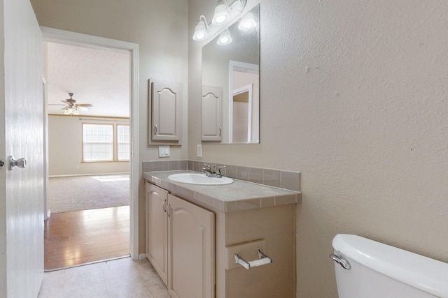 bathroom with a textured wall, toilet, ceiling fan, vanity, and tile patterned floors