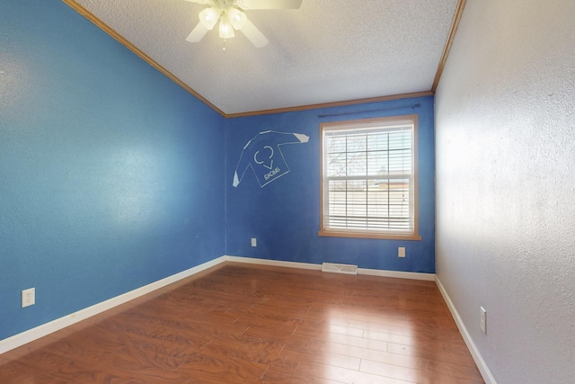 empty room with visible vents, ornamental molding, a textured ceiling, wood finished floors, and baseboards