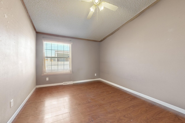 spare room with a textured ceiling, wood finished floors, visible vents, baseboards, and crown molding