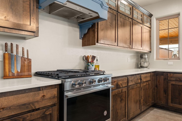 kitchen with light countertops, glass insert cabinets, dark brown cabinets, stainless steel gas range, and extractor fan