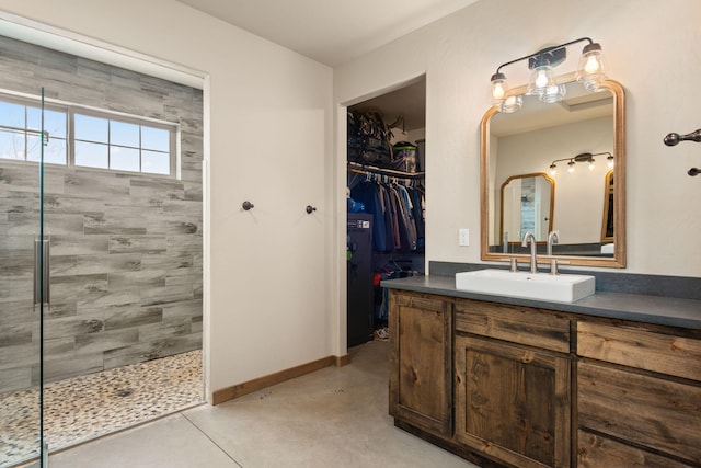1800 Los Pinos Rd, Bosque Farms, NM 87068 - bathroom with a tile shower, vanity, a walk in closet, baseboards, and concrete flooring