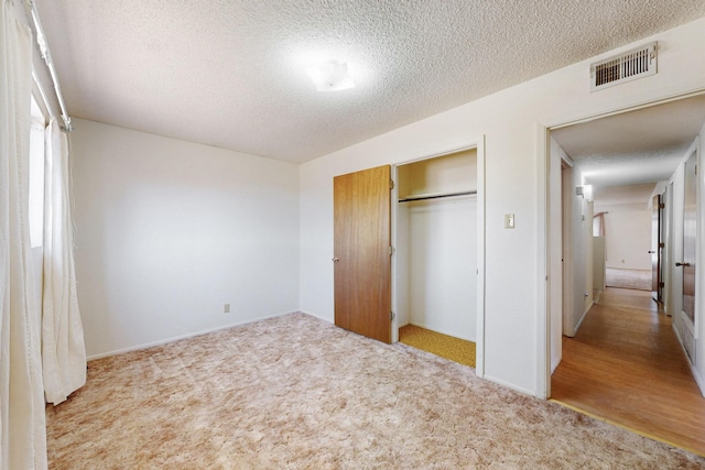 unfurnished bedroom with a textured ceiling, a closet, visible vents, and carpet flooring