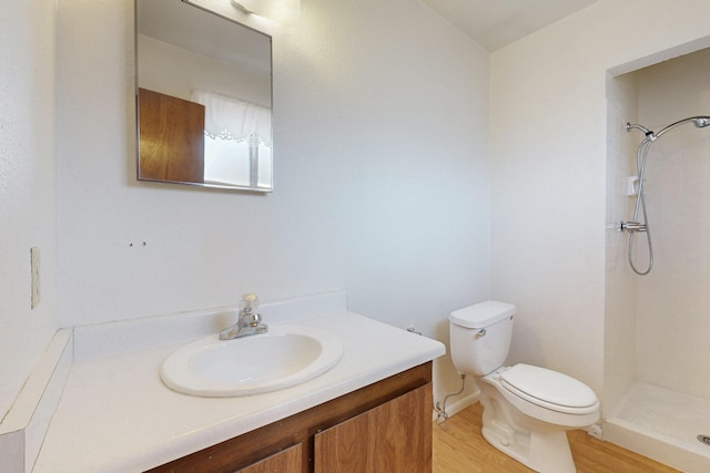 bathroom with wood finished floors, tiled shower, vanity, and toilet