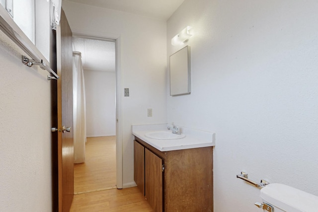 half bathroom with toilet, wood finished floors, and vanity