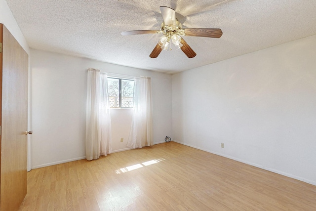 empty room with a textured ceiling, light wood finished floors, a ceiling fan, and baseboards