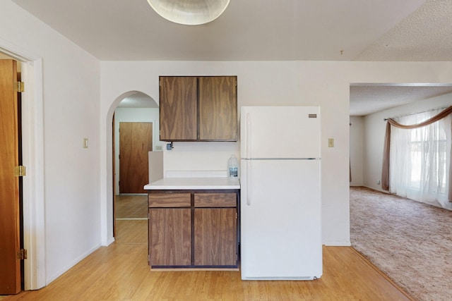 kitchen with arched walkways, a textured ceiling, light wood-style flooring, light countertops, and freestanding refrigerator