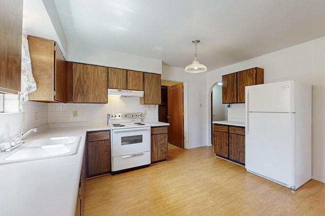 kitchen featuring arched walkways, light wood-style flooring, under cabinet range hood, white appliances, and a sink