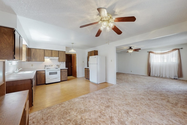 kitchen with white appliances, a sink, open floor plan, light countertops, and brown cabinets