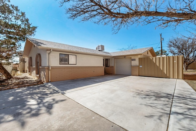 ranch-style home featuring brick siding, concrete driveway, an attached garage, fence, and stucco siding