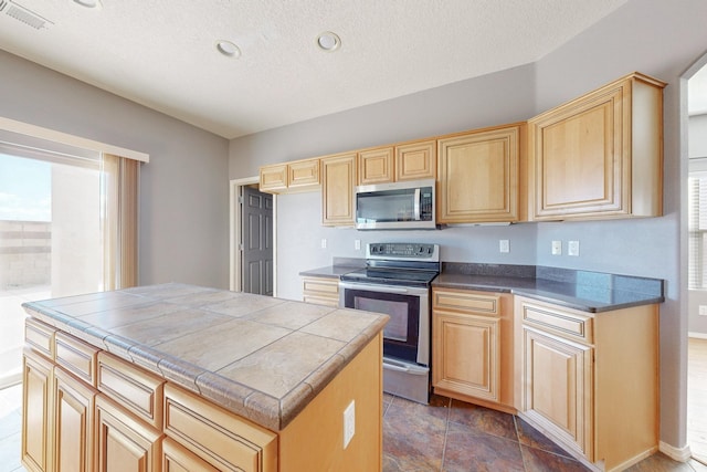 kitchen with appliances with stainless steel finishes, tile counters, visible vents, and light brown cabinetry