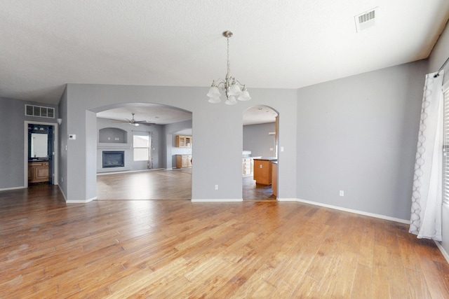 unfurnished living room featuring light wood-style floors, visible vents, arched walkways, and a glass covered fireplace