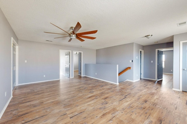 empty room with visible vents, light wood-style flooring, baseboards, and a textured ceiling