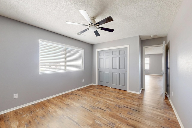 unfurnished bedroom featuring a closet, light wood-style flooring, baseboards, and a textured ceiling