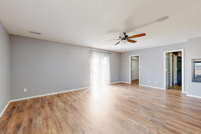 spare room with a textured ceiling, a ceiling fan, visible vents, baseboards, and light wood finished floors