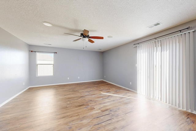 spare room featuring baseboards, visible vents, a ceiling fan, a textured ceiling, and light wood-type flooring