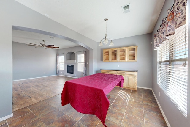 bedroom with arched walkways, ceiling fan with notable chandelier, visible vents, baseboards, and a glass covered fireplace