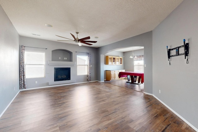 unfurnished living room with a textured ceiling, wood finished floors, a ceiling fan, baseboards, and a glass covered fireplace