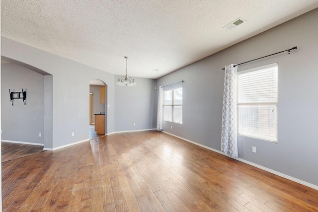 empty room featuring arched walkways, wood-type flooring, visible vents, and an inviting chandelier