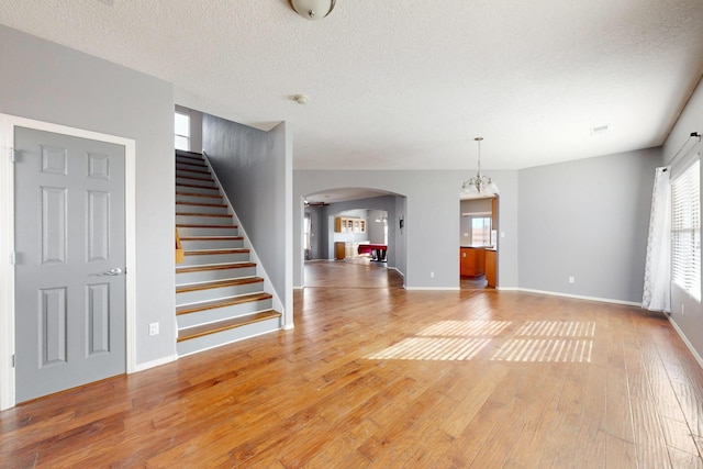 unfurnished living room featuring light wood finished floors, stairs, arched walkways, and a textured ceiling