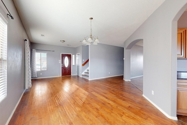 foyer entrance featuring arched walkways, light wood-style flooring, baseboards, stairs, and an inviting chandelier