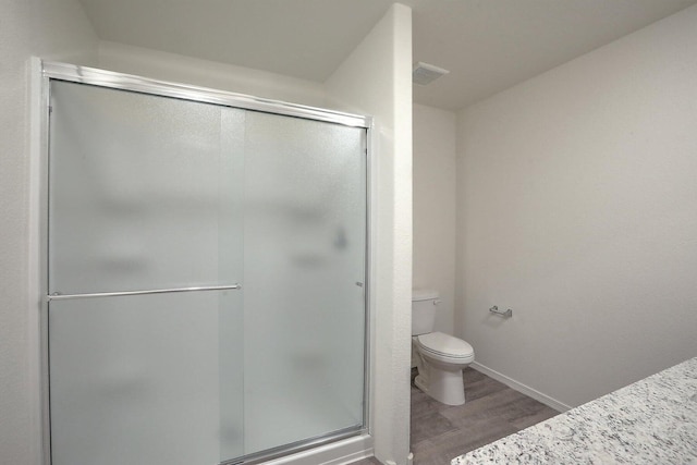 full bathroom with a stall shower, wood finished floors, toilet, and baseboards