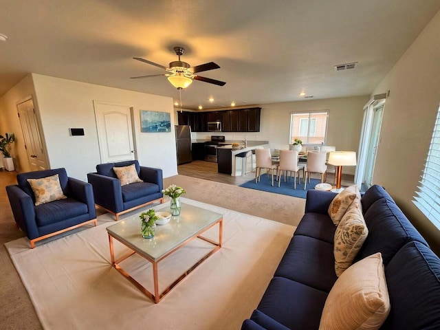 living area with ceiling fan, visible vents, and light colored carpet