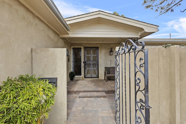 view of exterior entry featuring a gate and stucco siding