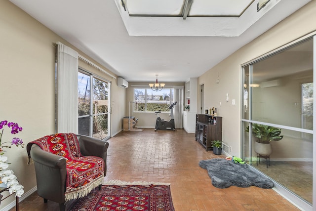 sitting room featuring a chandelier, a wall mounted AC, brick floor, and baseboards