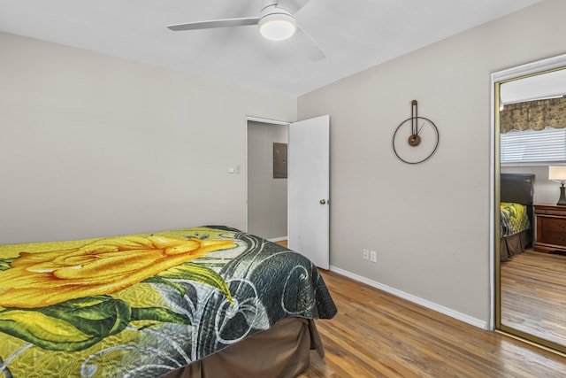 bedroom featuring ceiling fan, electric panel, baseboards, and wood finished floors