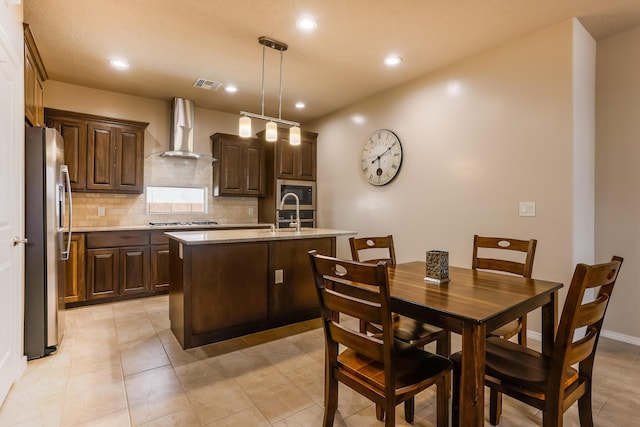 kitchen featuring wall chimney range hood, visible vents, appliances with stainless steel finishes, and dark brown cabinets